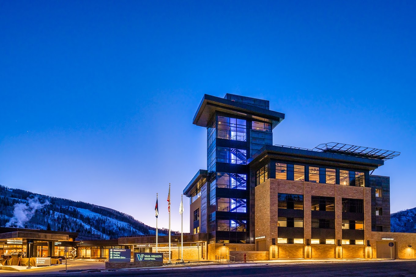 Vail Valley Medical Center at dusk, with the sunset peaking over the horizon behind the building, lit up by its own evening lights